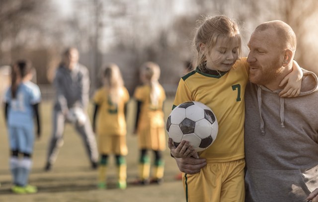 Middle Aged Redhead Father and blonde daughter coaching soccer together to a Girl Football team