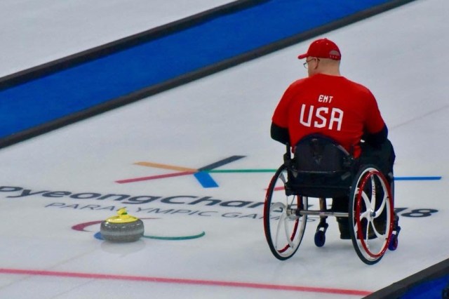 Wheelchair curler Steve Emt in action on the ice next to curling stone