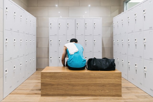 Man with towel sitting on wooden bench in gym.