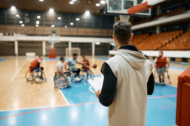 Rear view of coach of basketball watching his team with disabilities playing the game during sports training on the court.