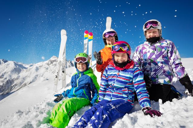 Family of four in the snow on a ski slop with bright ski jackets and skis sticking up in the snow