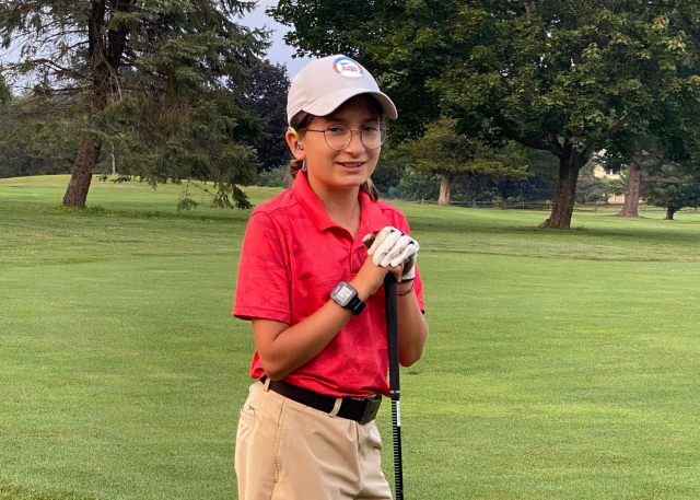 Betty Glyptis poses on the golf course with a club and hat wearing a pink golf polo