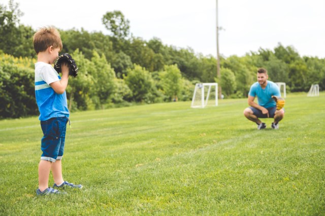 Dad with his little son are playing baseball on green grassy lawn
