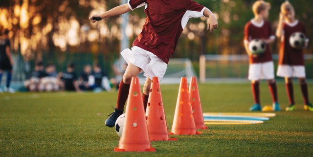 Boy in red soccer jersey shirt running with ball between cones