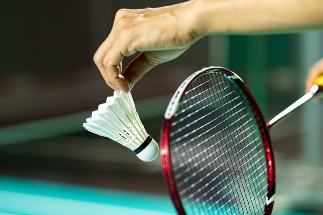 Hands of BADMINTON player holding racket serving white new shuttlecock with blur Badminton court background, popular indoor sport concept