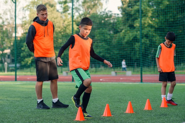 Motivated sporty 13-s boys in orange vests running among the plastic cones during soccer training at the stadium.