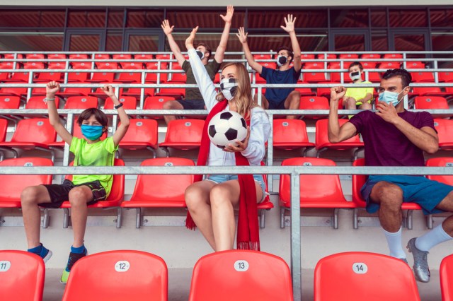 Fans watching football match under social distancing measures in stadium wearing masks