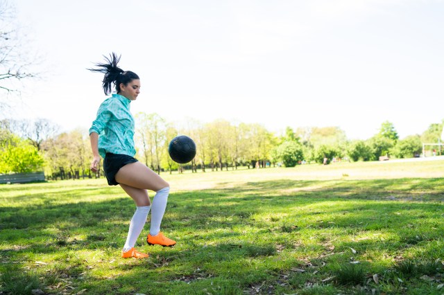 Portrait of young woman practicing soccer skills and doing tricks with the football ball. Soccer player juggling the ball. Sports concept.
