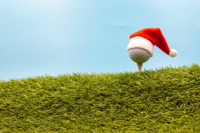 Golf ball on tee pin with Santa hat is on blue sky background ready to tee off for Christmas Holiday