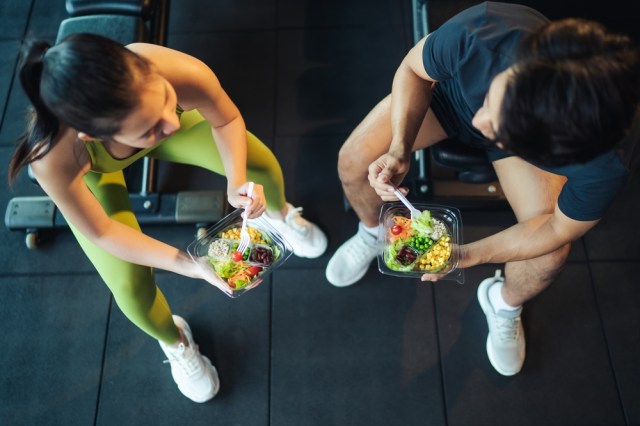 Man and woman athlete's eating in gym.