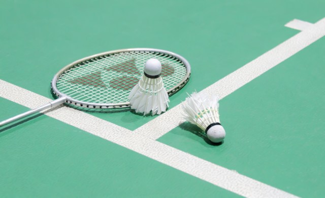 White badminton shuttlecock on a green floor with blurred players in badminton court