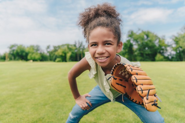 portrait of smiling little girl with baseball glove playing baseball in park