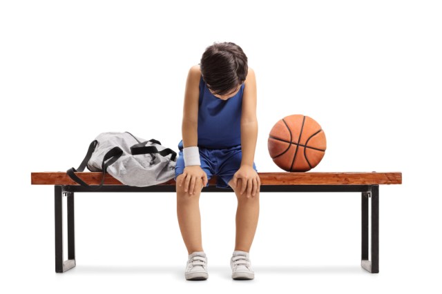 Sad little basketball player sitting on a bench isolated on white background