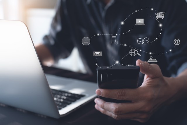 Why Being Active on Google and Facebook is Critical for Your Business: Person at computer with phone in hand