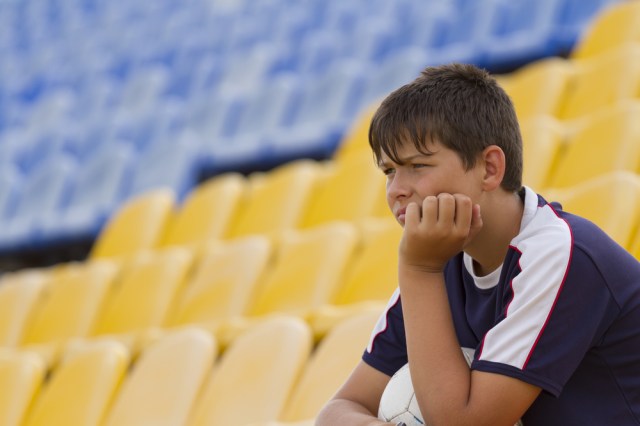 Young soccer player with a ball watching from the stands at the game.